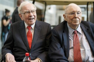 Warren Buffett and Charlie Munger on the back of a golf cart at a Berkshire Hathaway annual meeting.